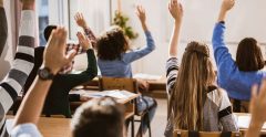 Rear view of large group of students raising their hands to answer the question on a class.